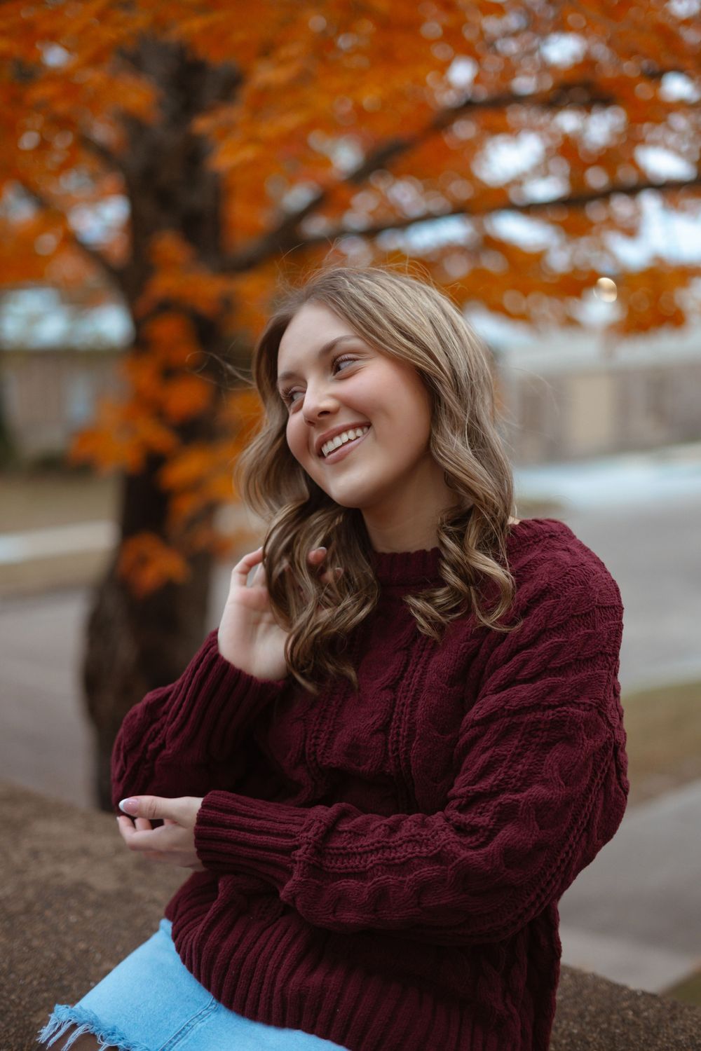 A cozy autumn scene with someone wearing a burgundy sweater against orange fall foliage.