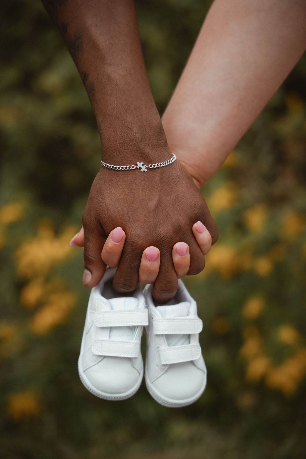Hands holding tiny white baby shoes against a background of yellow flowers.