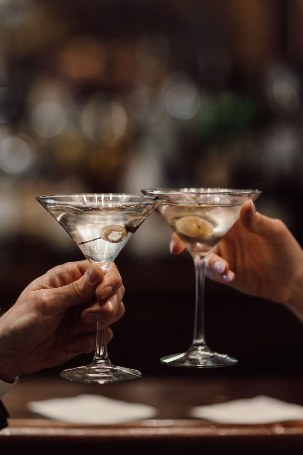 Hands holding martini glasses in a dimly lit bar atmosphere.
