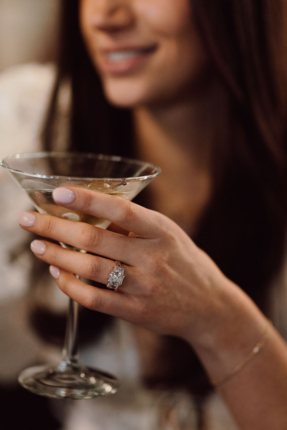 Close-up of hands holding a martini glass with an elegant diamond ring on display.