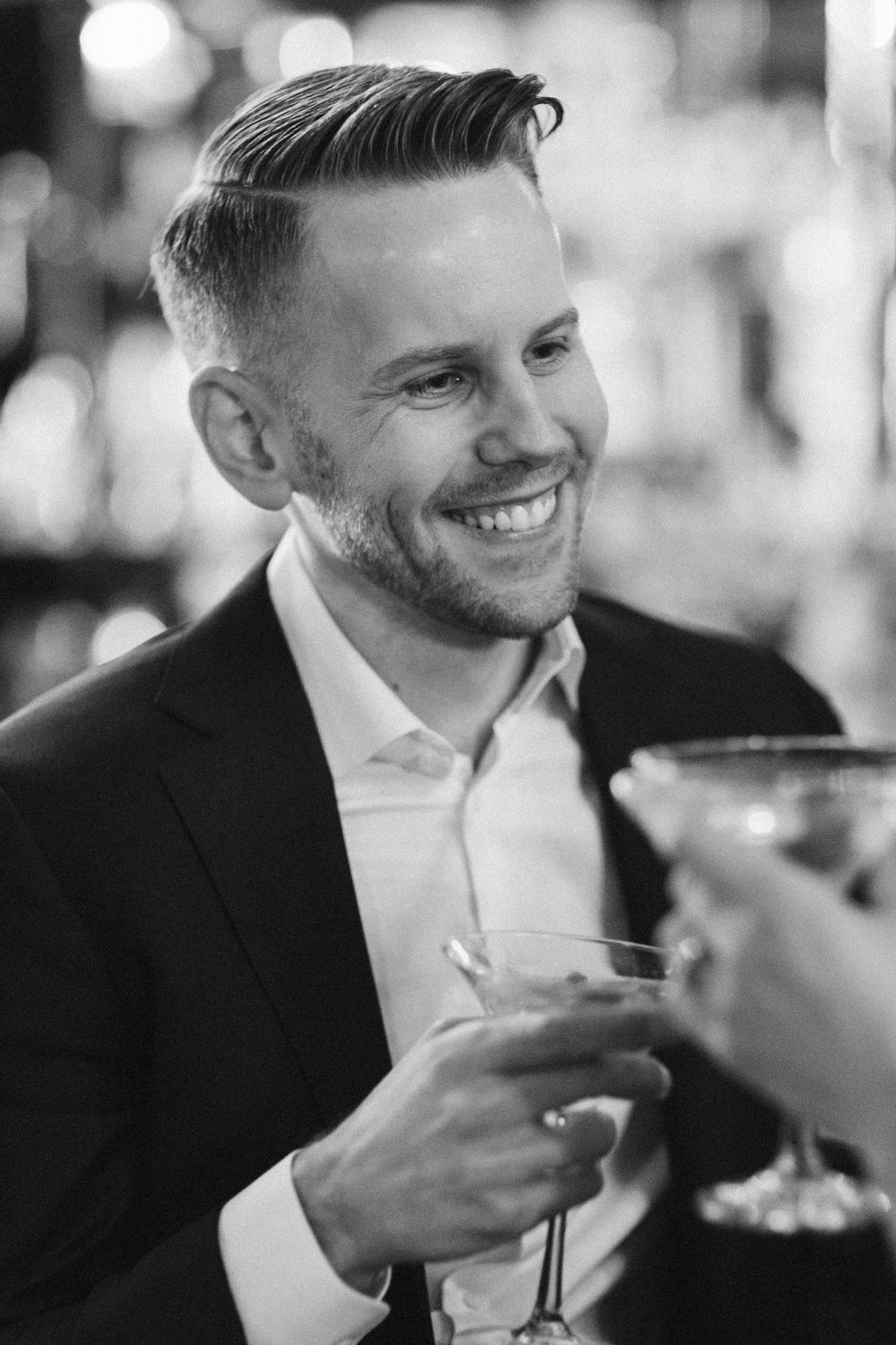 Person in black suit holding martini glass during elegant evening celebration.