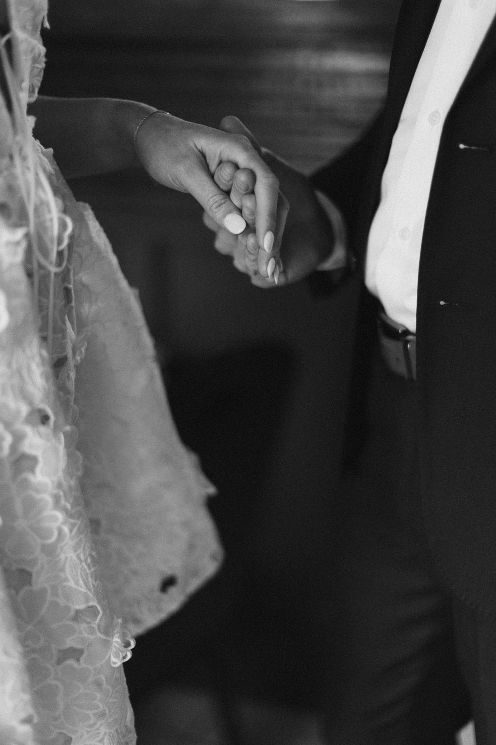 Close-up detail of a white lace wedding dress against a dark background.