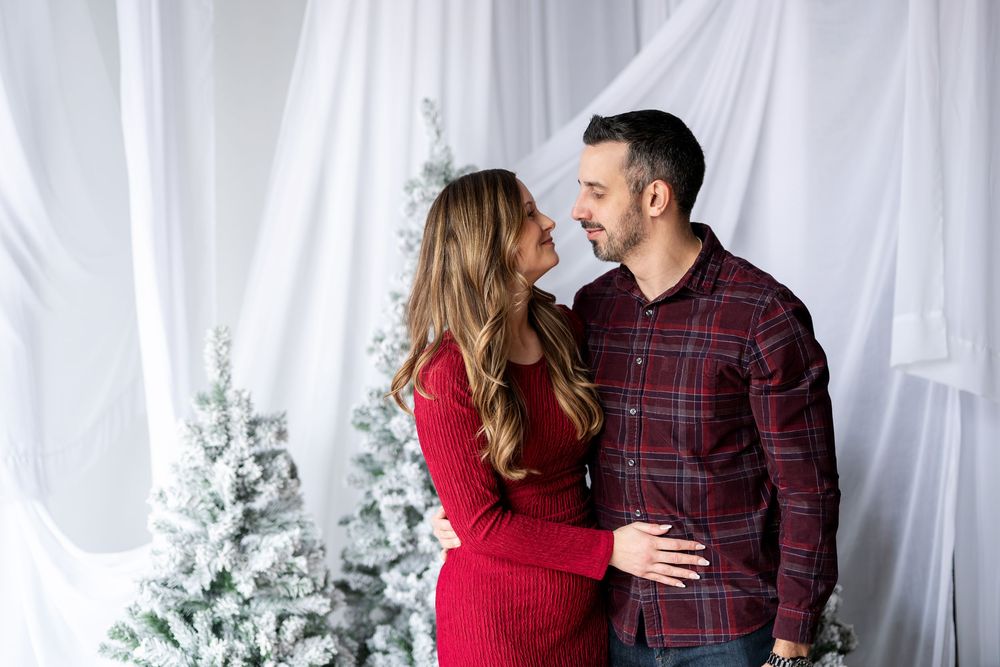Happy couple gazing at each other and smiling near decorated snow-flocked Christmas trees in a studio setting.