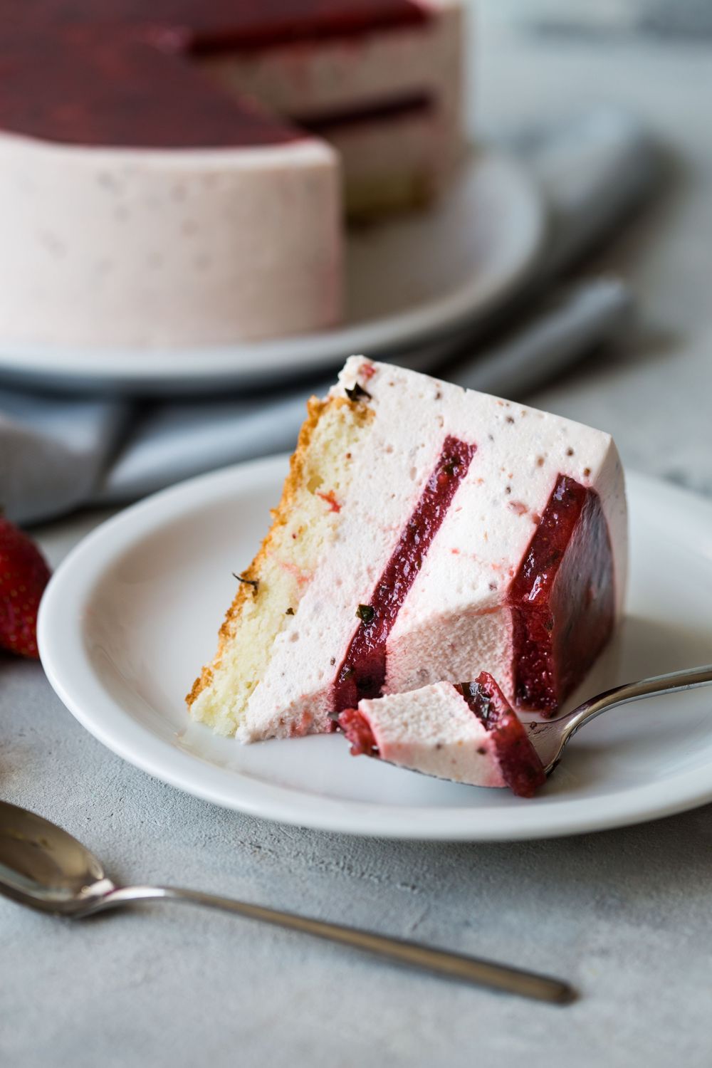 A slice of layered strawberry mousse cake with pink and red layers on a white plate with a silver fork.