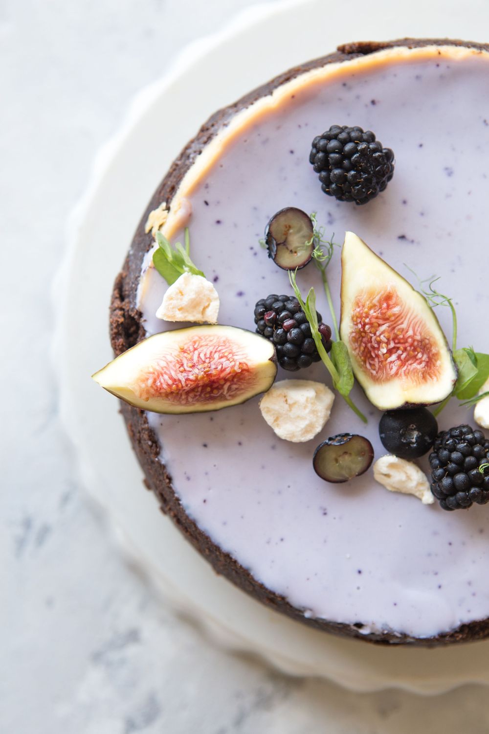 A white plate with fresh figs, blackberries and cream garnished with herbs on a marble surface.