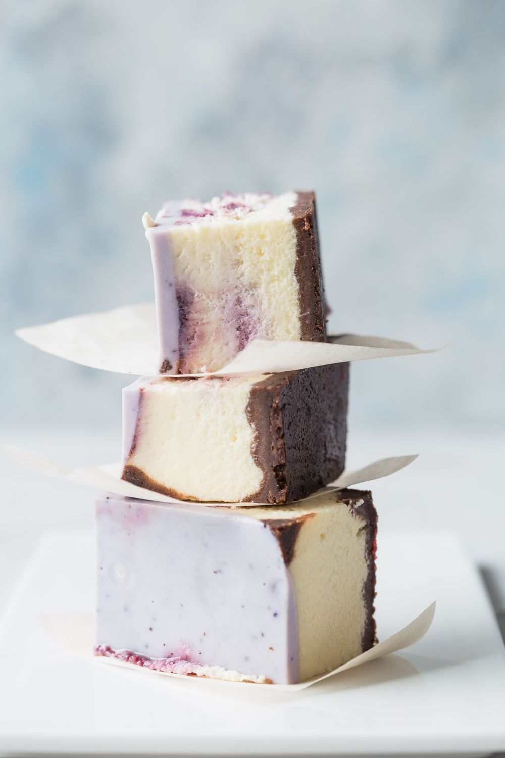 Homemade marshmallows with purple swirls stacked in pairs on a white surface against a light blue background.