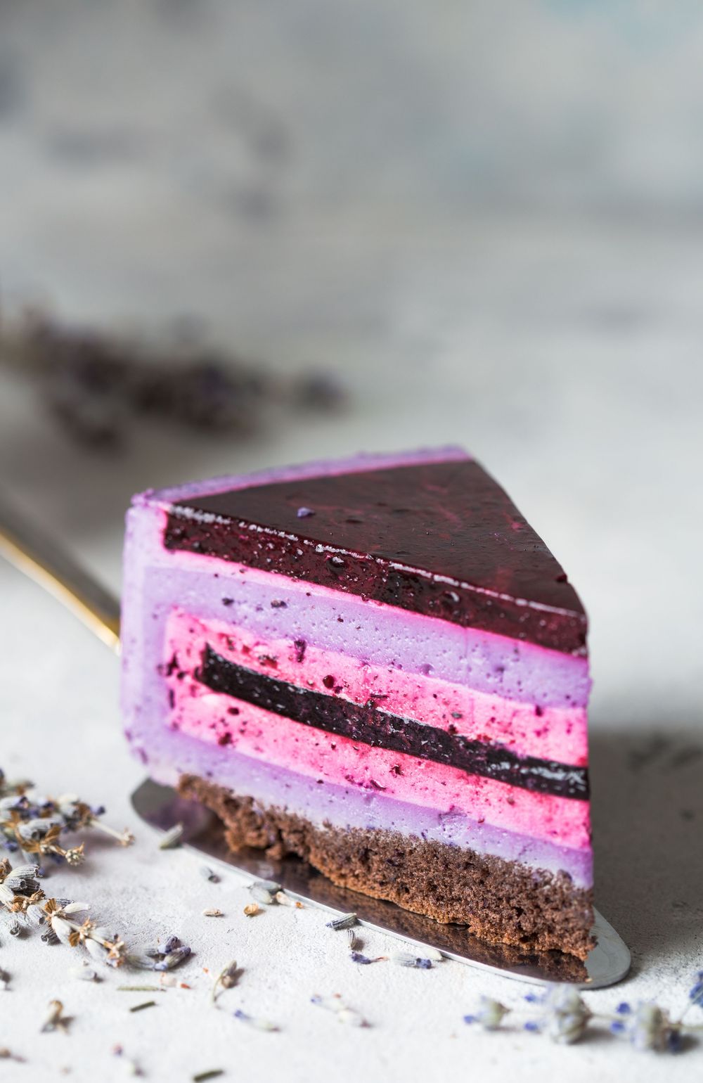 Slices of layered chocolate and pink dessert with dark chocolate ganache topping and crumbs on a marble surface.