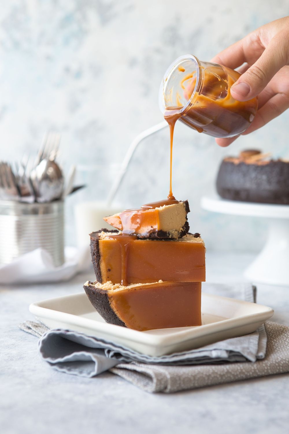 Caramel sauce being poured over a chocolate dessert slice on a white plate against a light gray background.