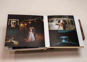 An open wedding photo album displays romantic evening photos with glowing lights and dance floor scenes.