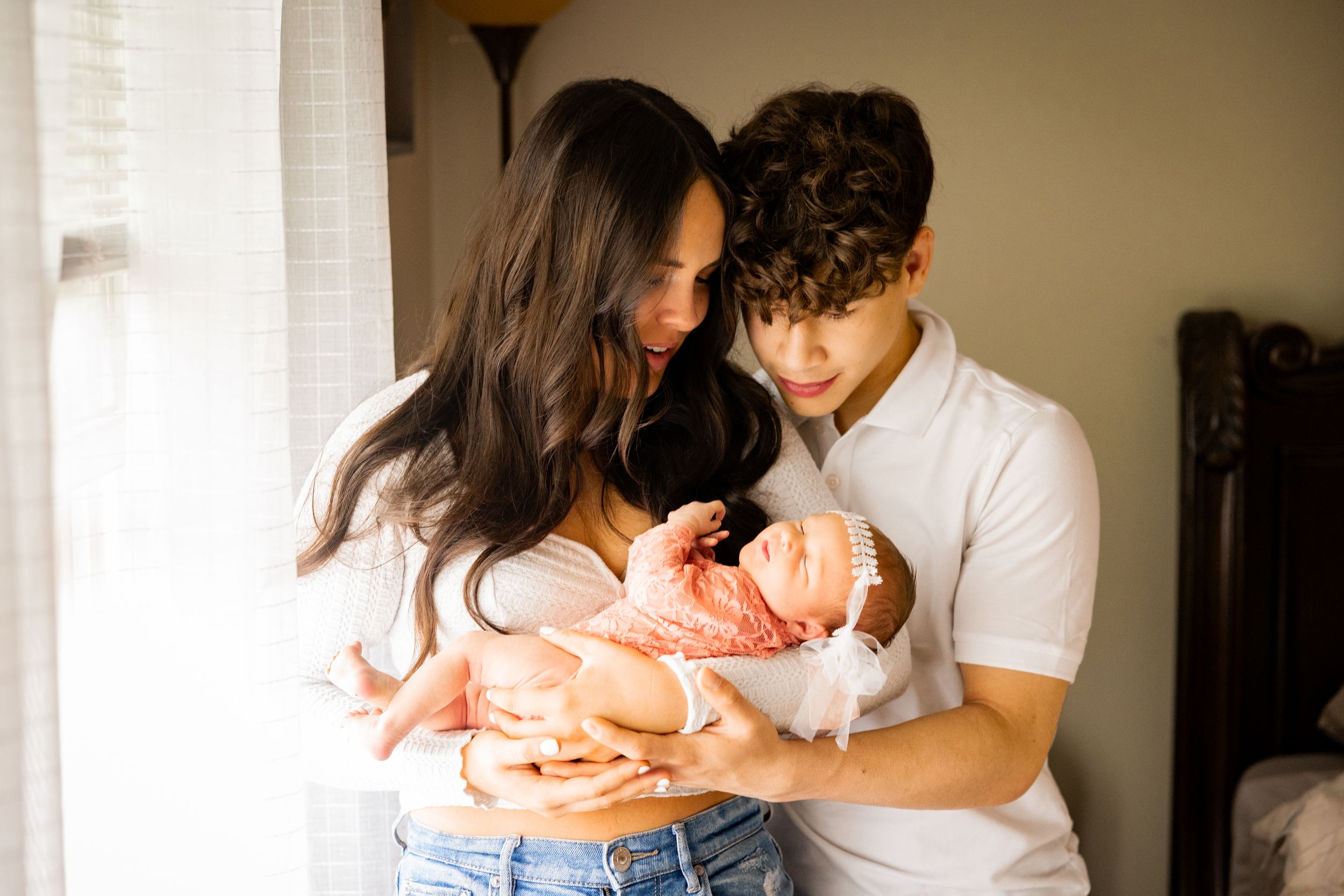 A family shares tender moments together while sitting on a bed in a sunlit room.