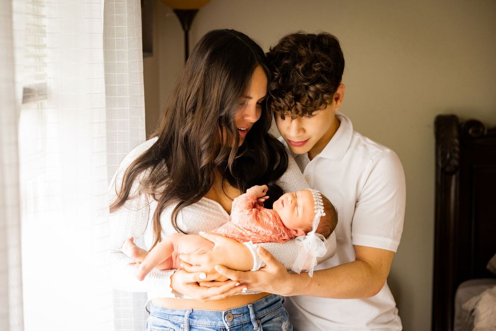 A family shares tender moments together while sitting on a bed in a sunlit room.