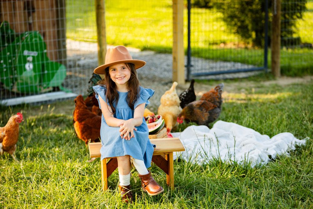 A person in a straw hat and denim sits on lush green grass with a brown and white dog on a sunny day.