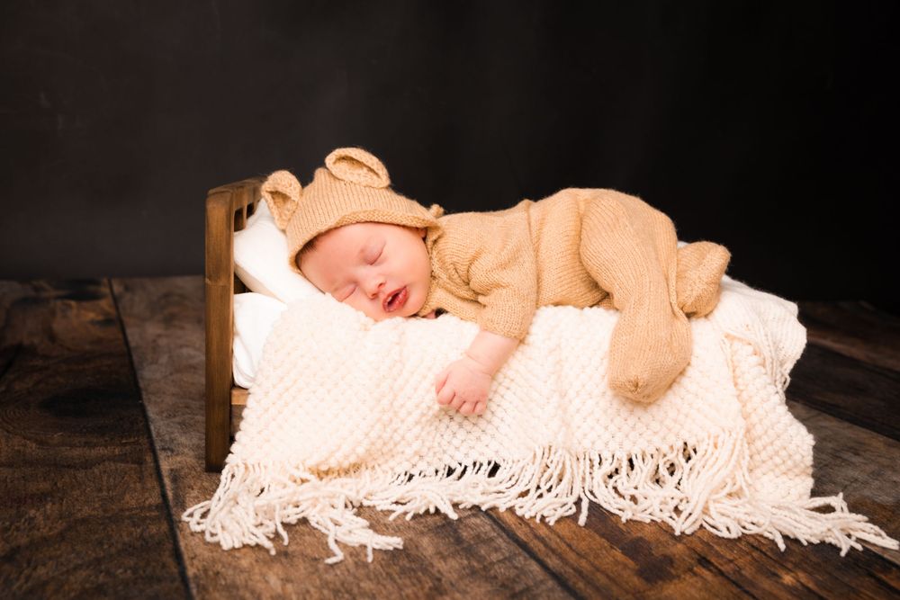 Newborn baby sleeping peacefully on white fringed blanket in rustic wooden setting.