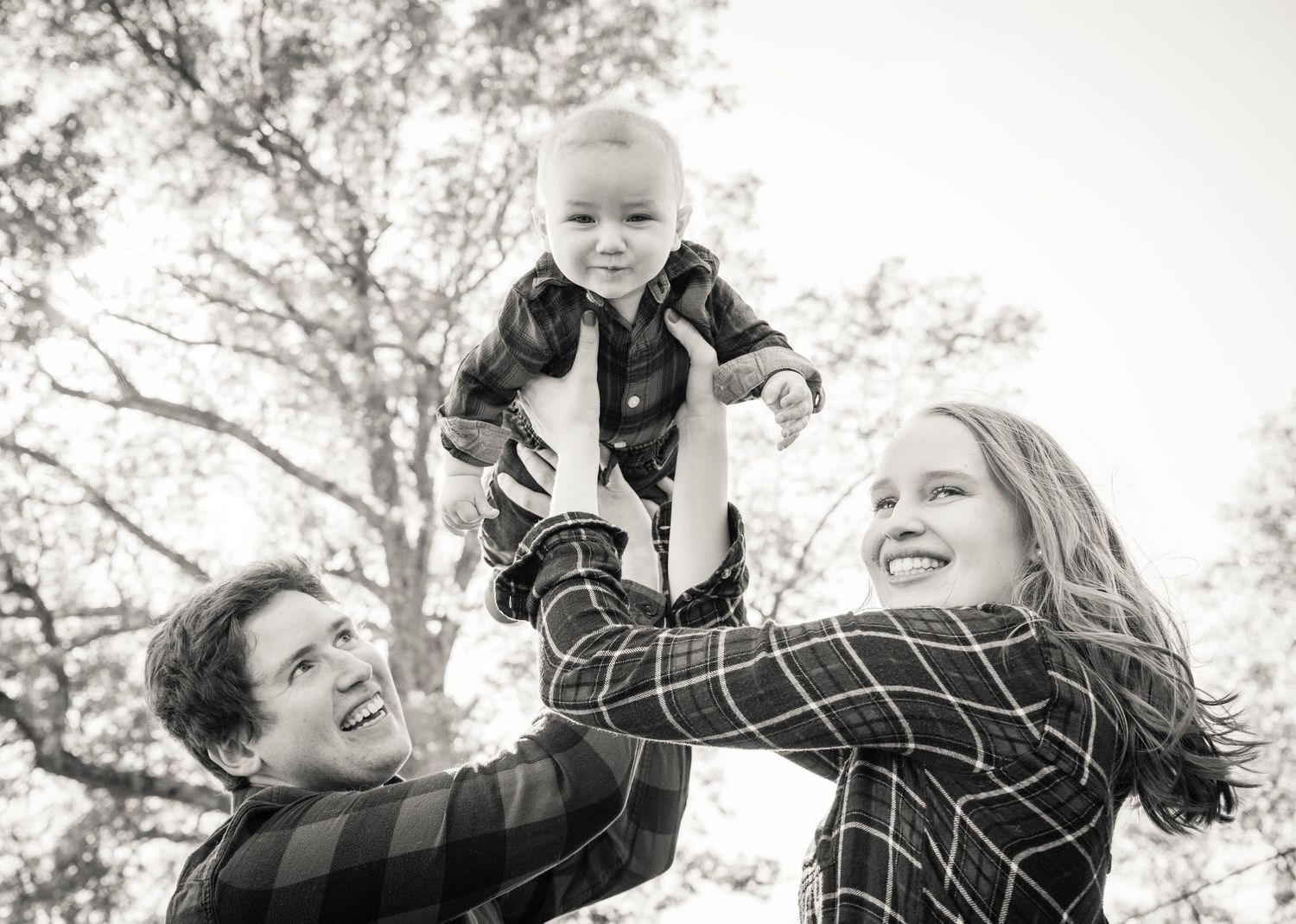 a couple hold their baby up in the air outdoors