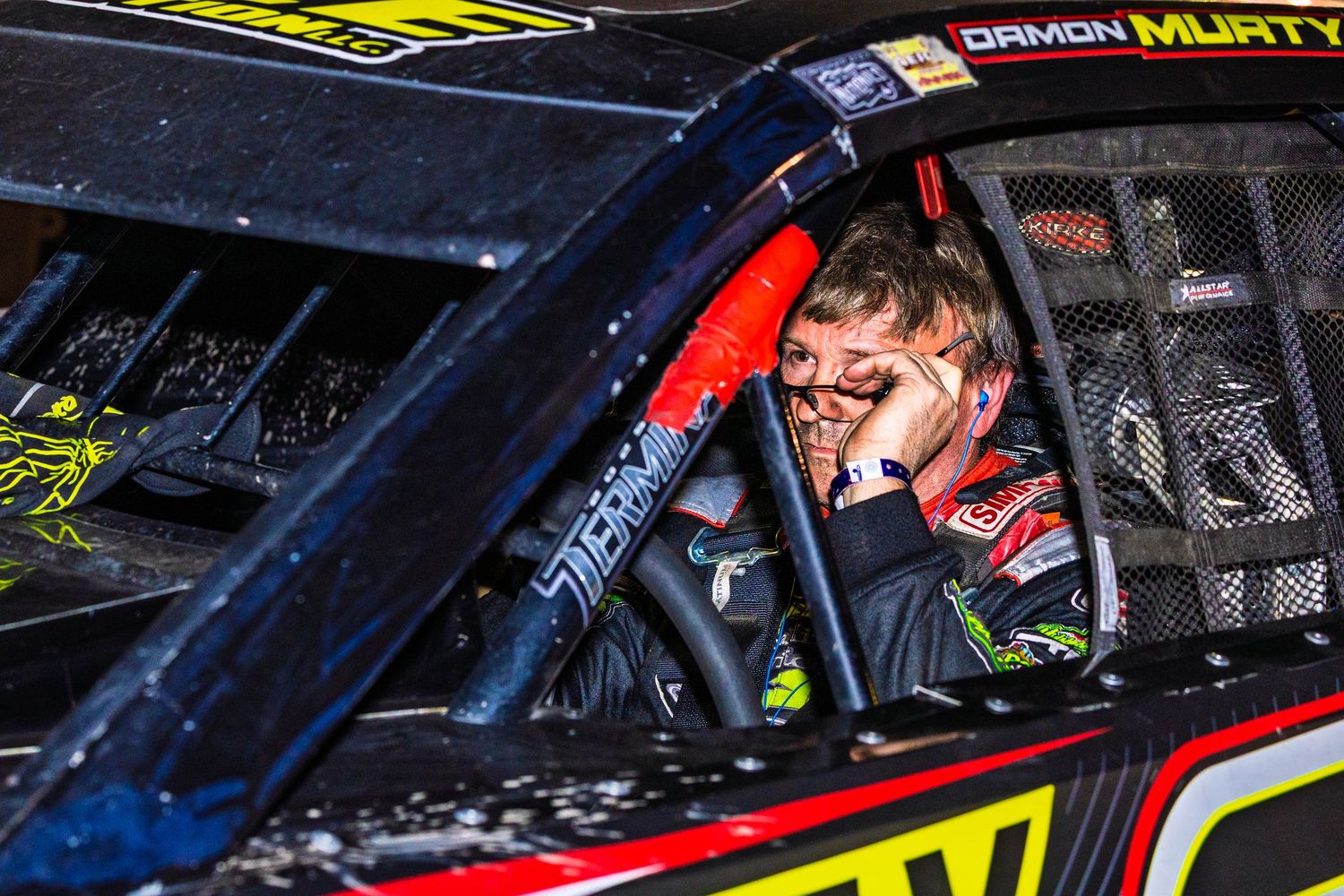 Race car driver sits in cockpit of NASCAR vehicle during competition at speedway track.