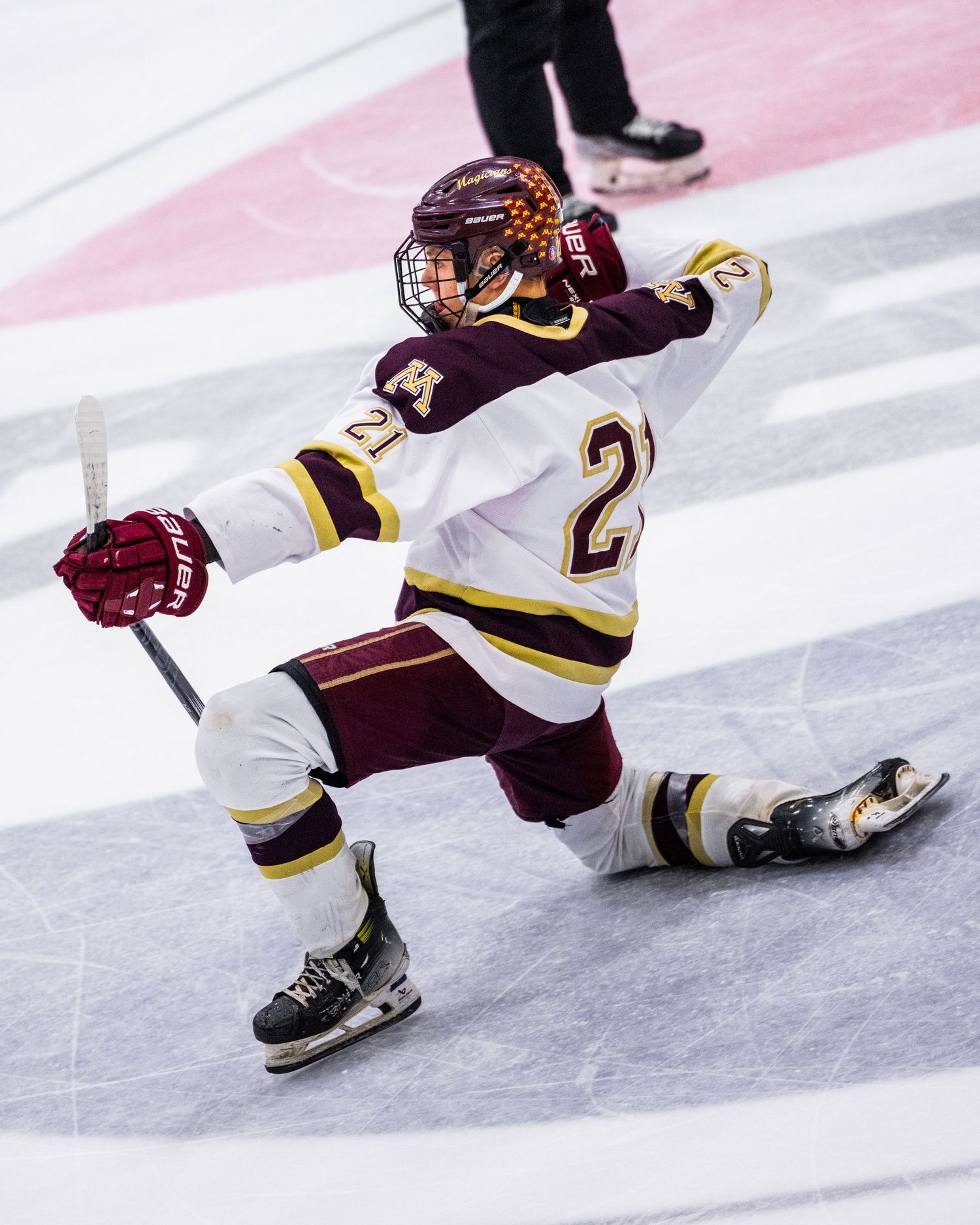Hockey player rests head and arms on rink boards during game break, wearing maroon and white uniform.