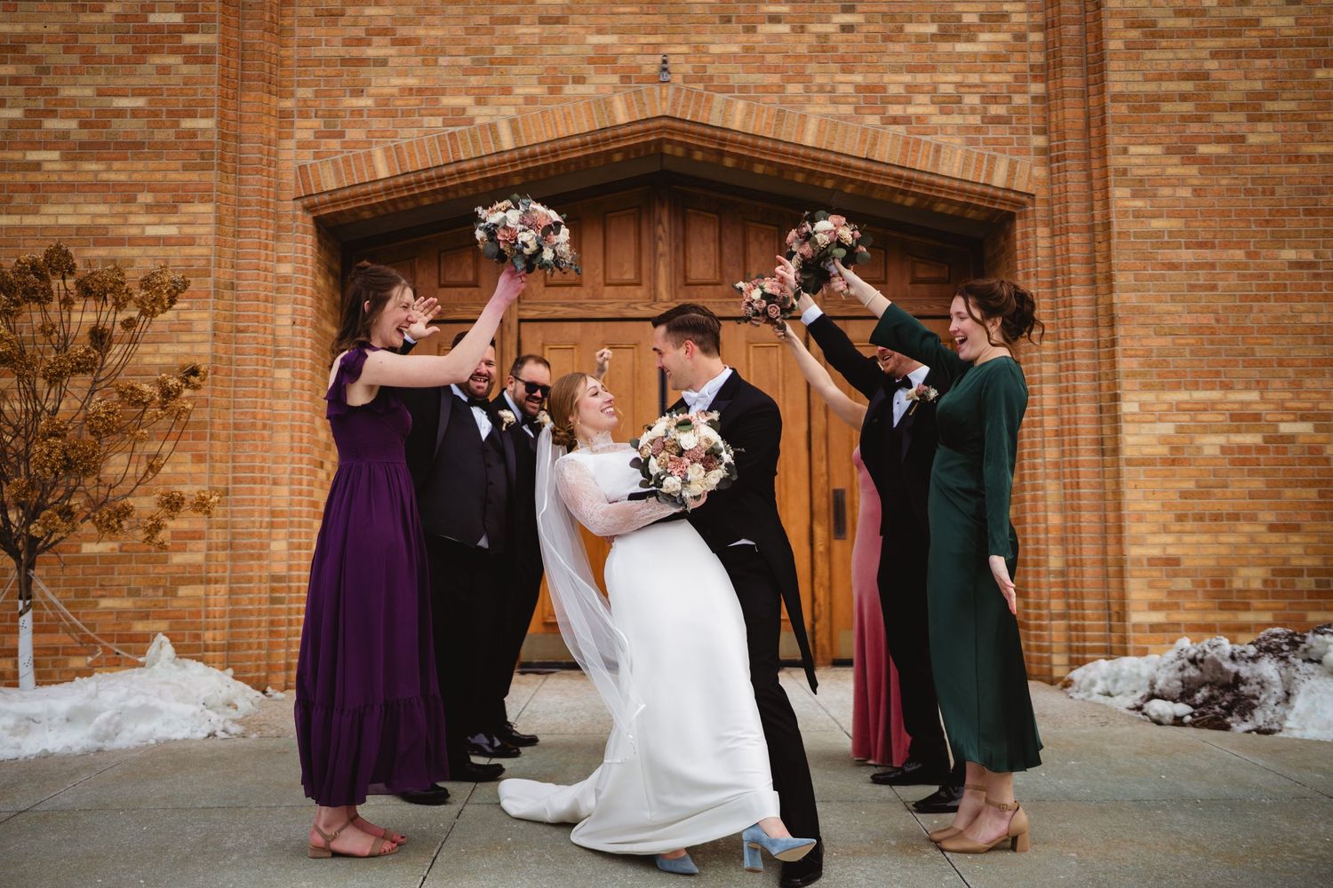 Wedding guests perform a synchronized dance routine in front of a rustic brick wall.
