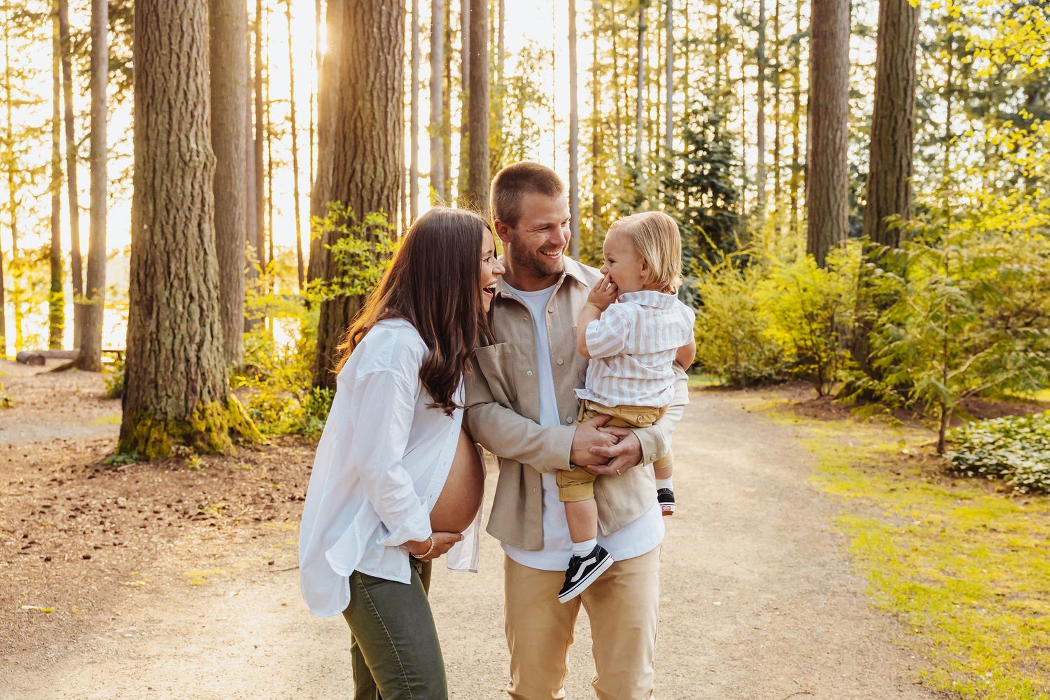 Two people walking along a scenic dirt path through a pine forest on a sunny day.