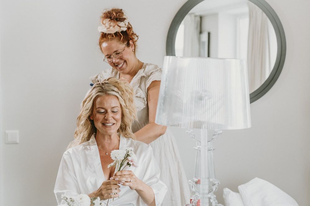 Brud sitter på en stol framför en spegel, och blir stylad av en stylist inför sitt bröllop.