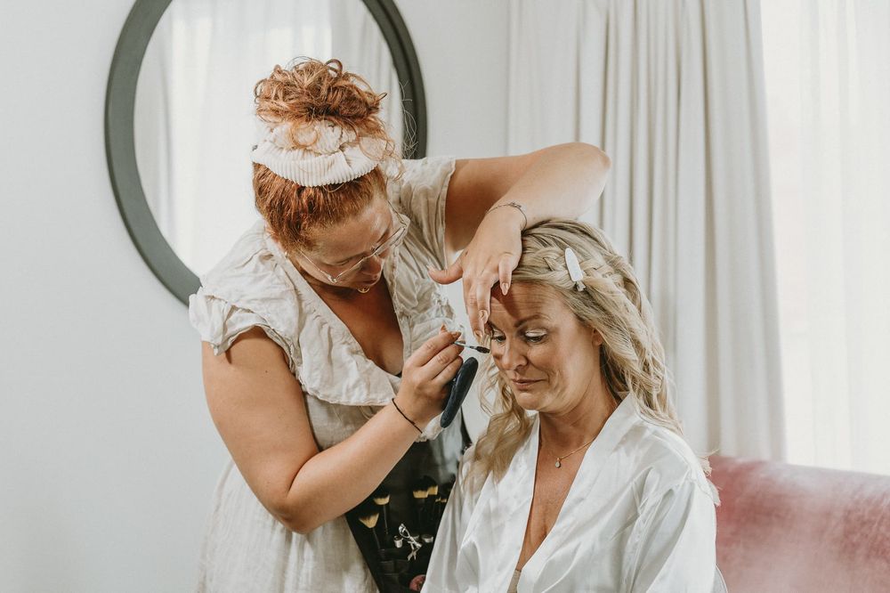 Brud sitter på en stol framför en spegel, och blir stylad av en stylist inför sitt bröllop.