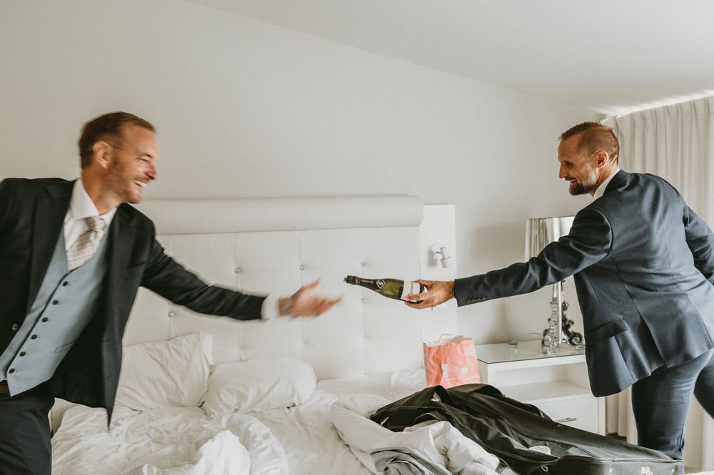 Bestman räcker över en flaska bubbel till brudgummen, i sviten på Marstrands Havshotell.