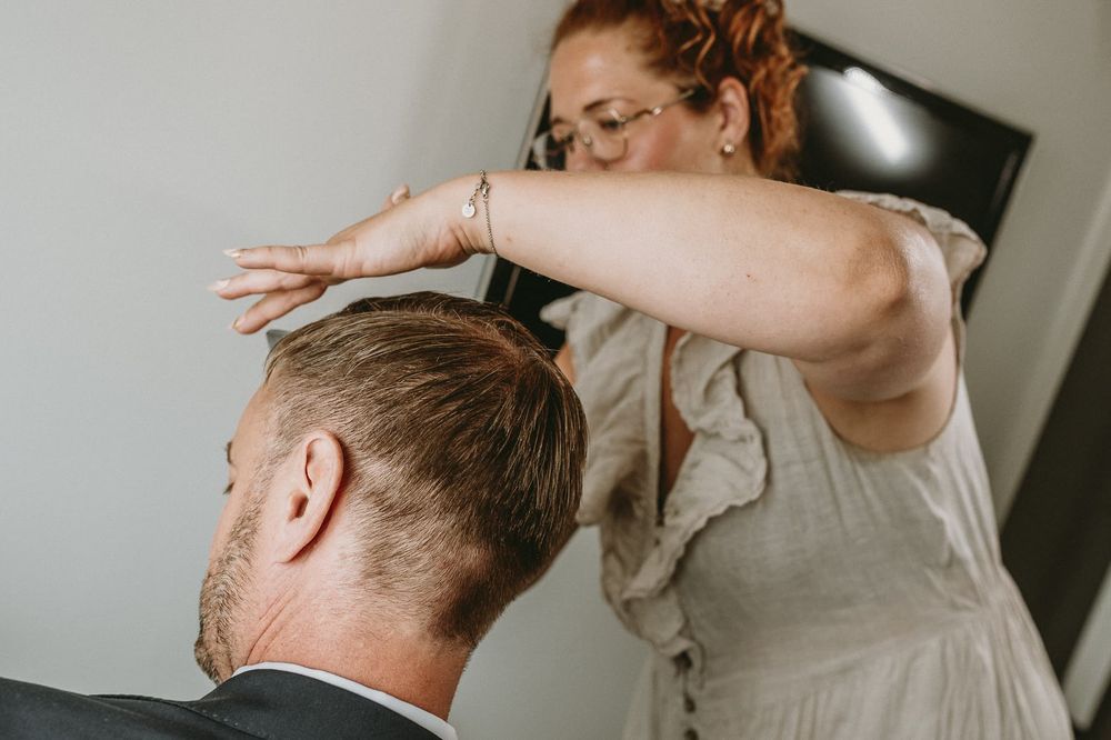 Brudgum får sitt hår stylat av stylist inför sitt bröllop. Han har blå kostym.