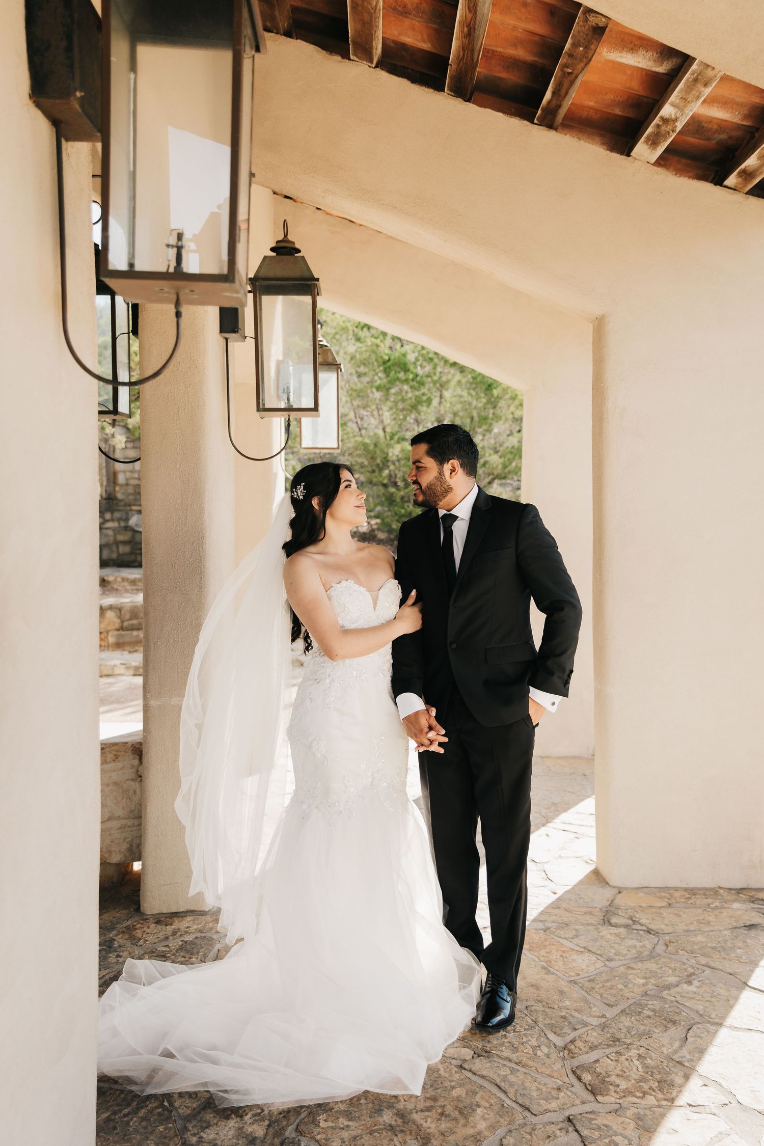 A romantic wedding couple dances together under a covered patio with white columns and stone flooring.