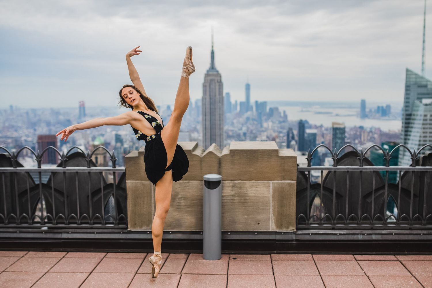 Ballerina performing arabesque on NYC rooftop with Empire State Building skyline backdrop.