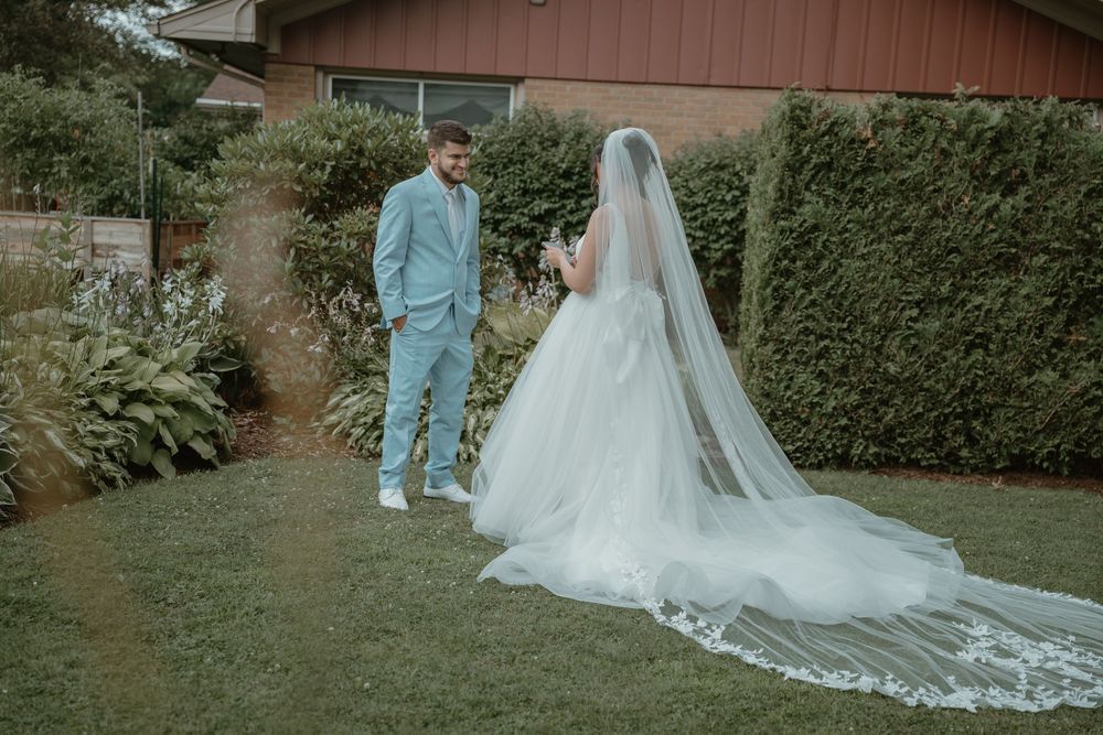 Groom in light blue suit sees his bride in a flowing white gown and cathedral veil for the first look.