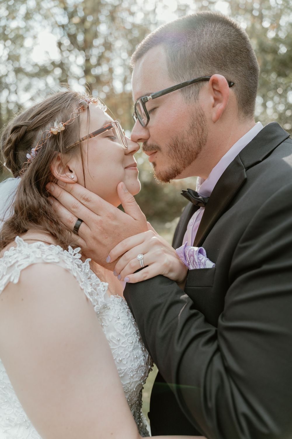 Bride and groom share an intimate almost-kiss moment, with groom tenderly holding bride's face outdoors.