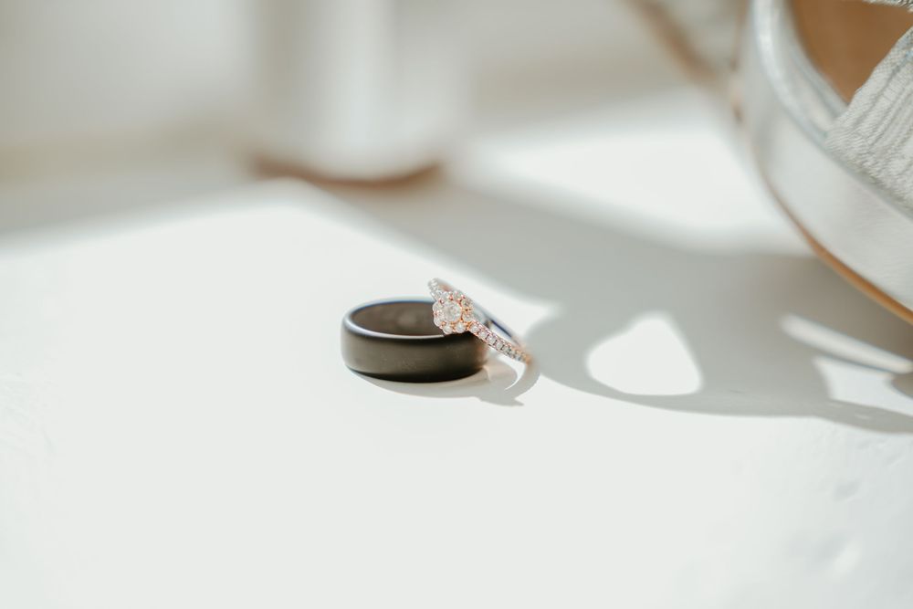 Close-up of wedding rings, a black tungsten band and diamond engagement ring, on a white surface with soft natural light.