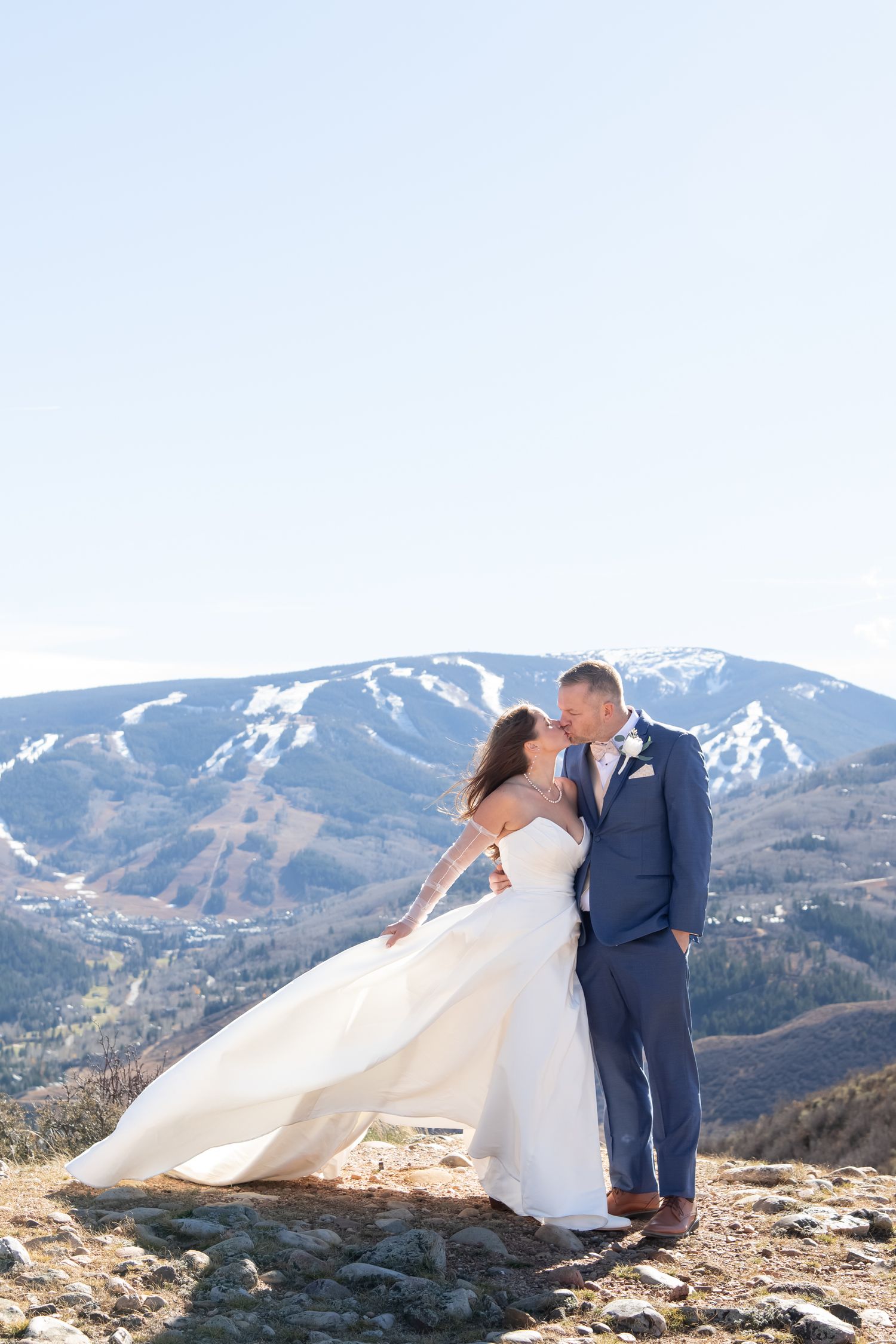 A couple in wedding attire embrace against a stunning mountain backdrop with golden fields and dramatic peaks in Beaver Creek Colorado.