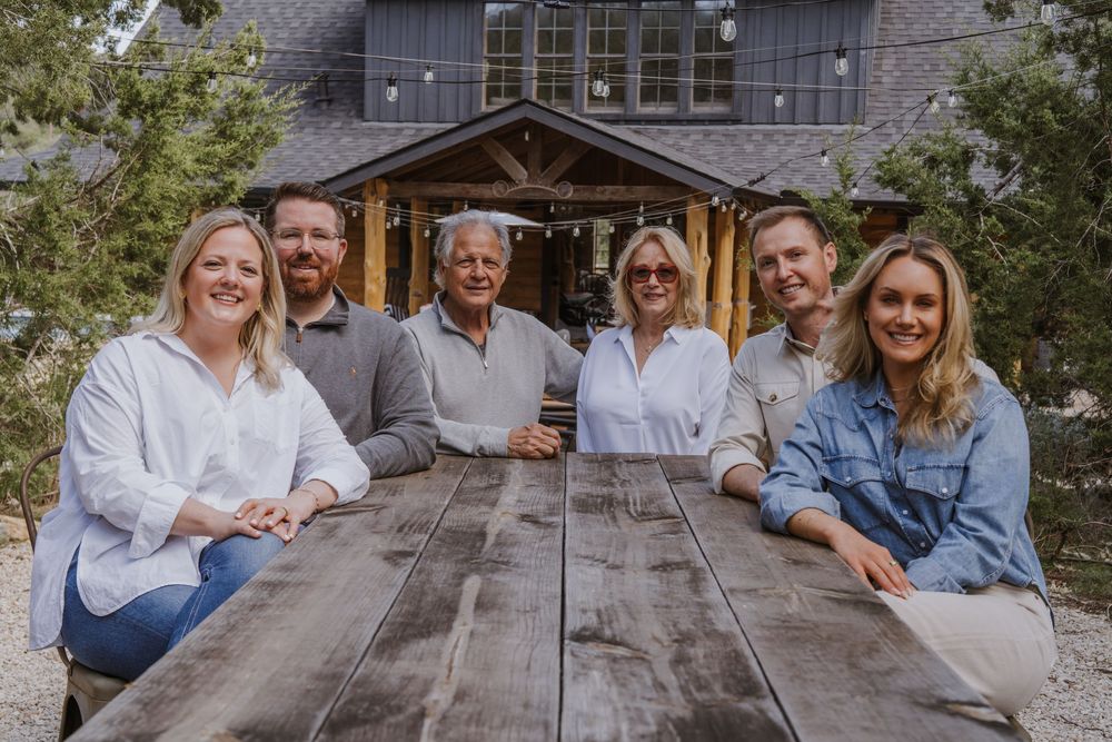 Family gathering around a rustic wooden table outside a cabin.