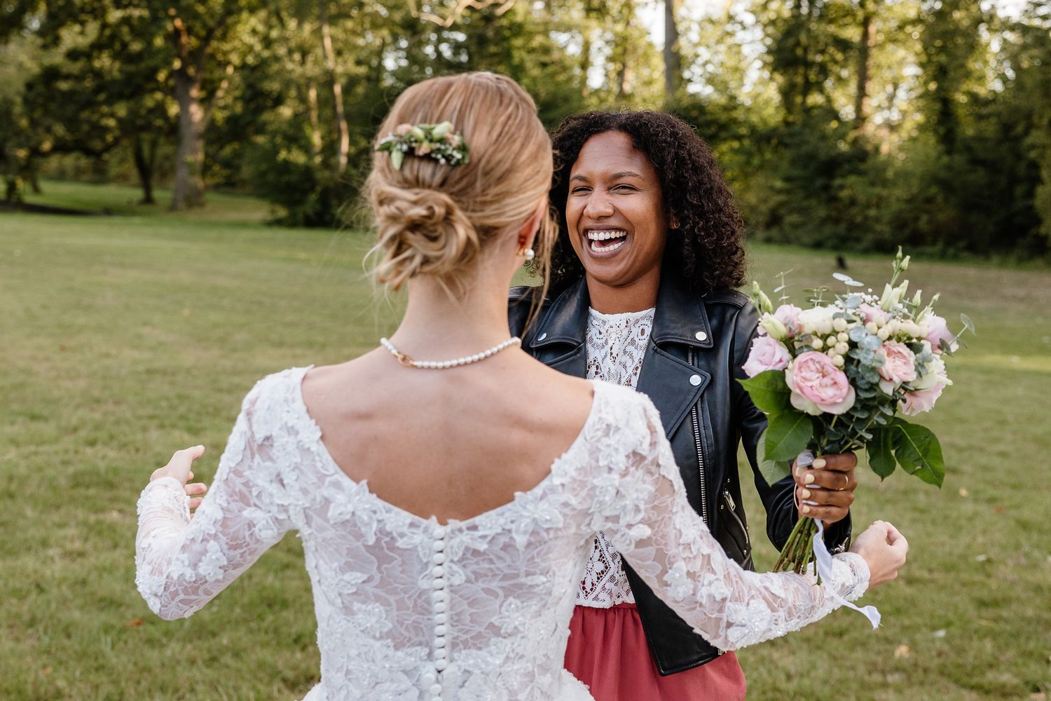 Reportage mariage Lille : capturer les emotions entre la mariee et son amie qui a attrape le bouquet dans le jardin du chateau du biez.