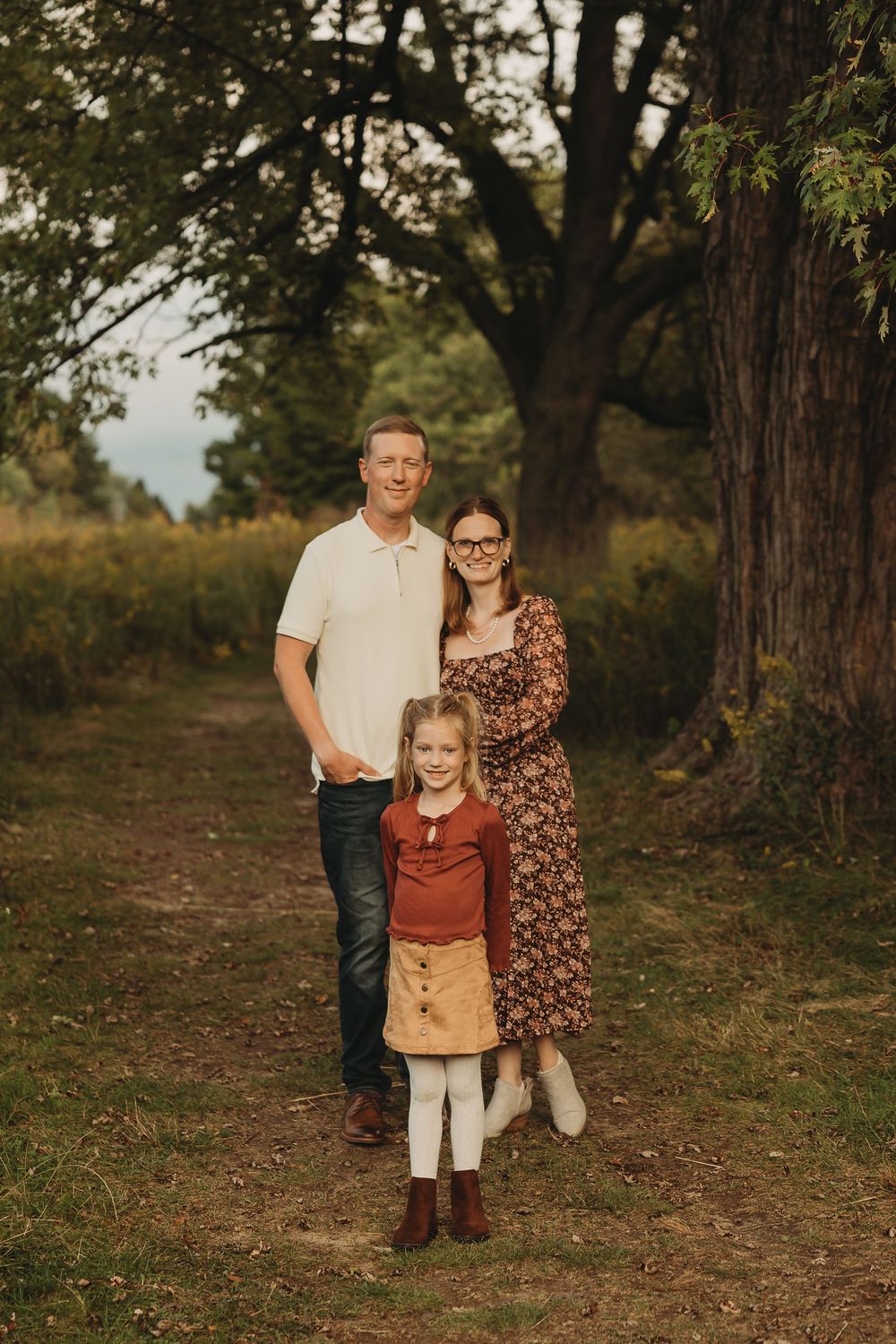 Family portrait session in a rustic outdoor setting with autumn trees and natural lighting.