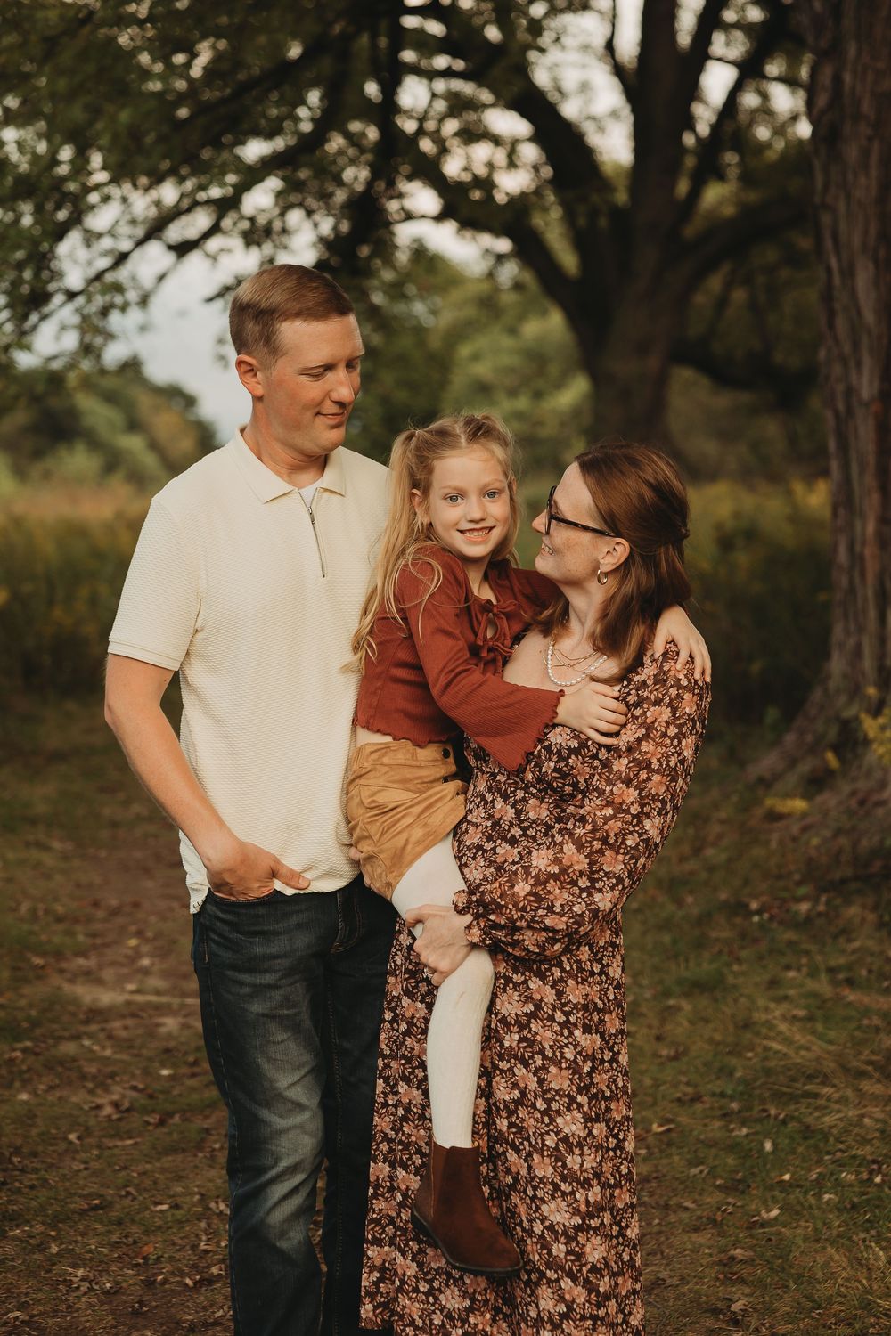 A family of three shares joyful moments together during an outdoor autumn photoshoot in a wooded setting.