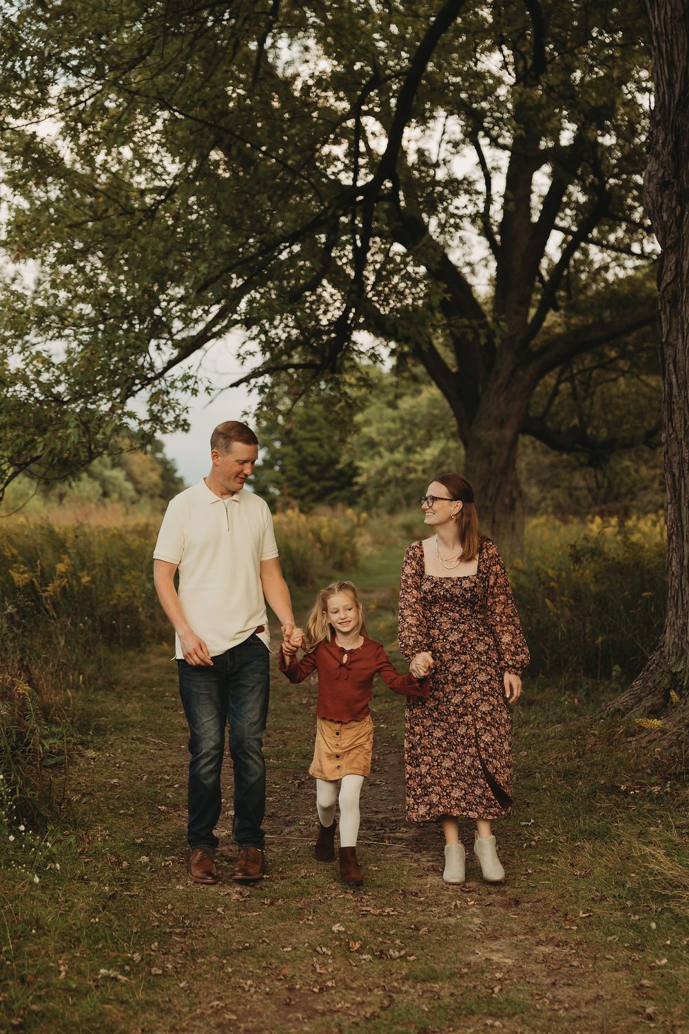 A family enjoys a casual stroll along a natural path surrounded by trees during an autumn evening photoshoot.
