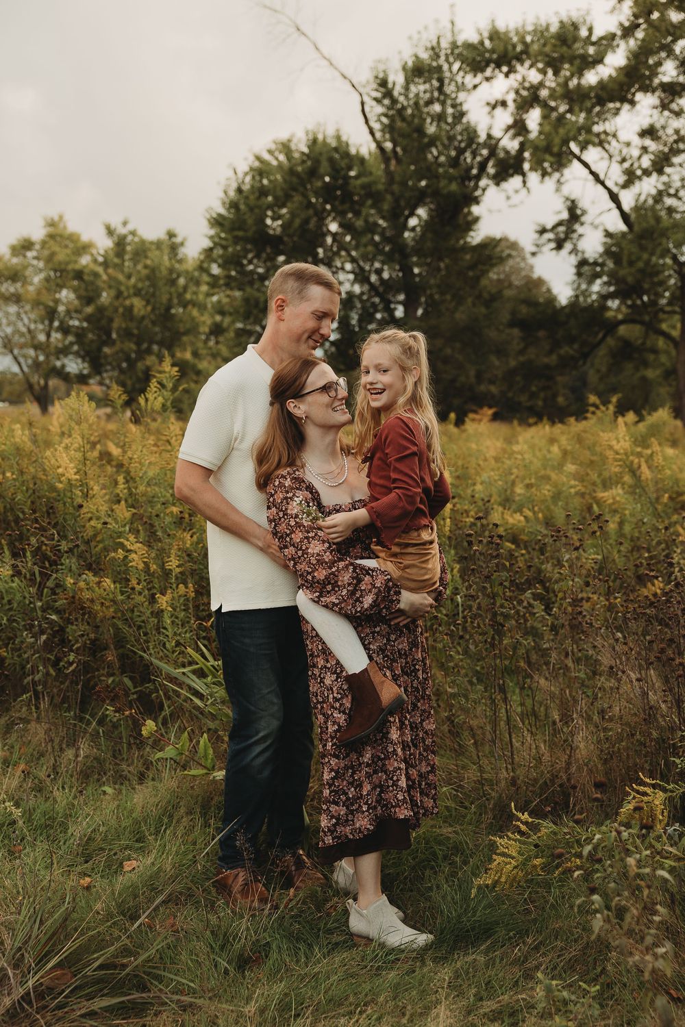 Family embraces together in a golden wildflower field during sunset while wearing coordinated outfits.
