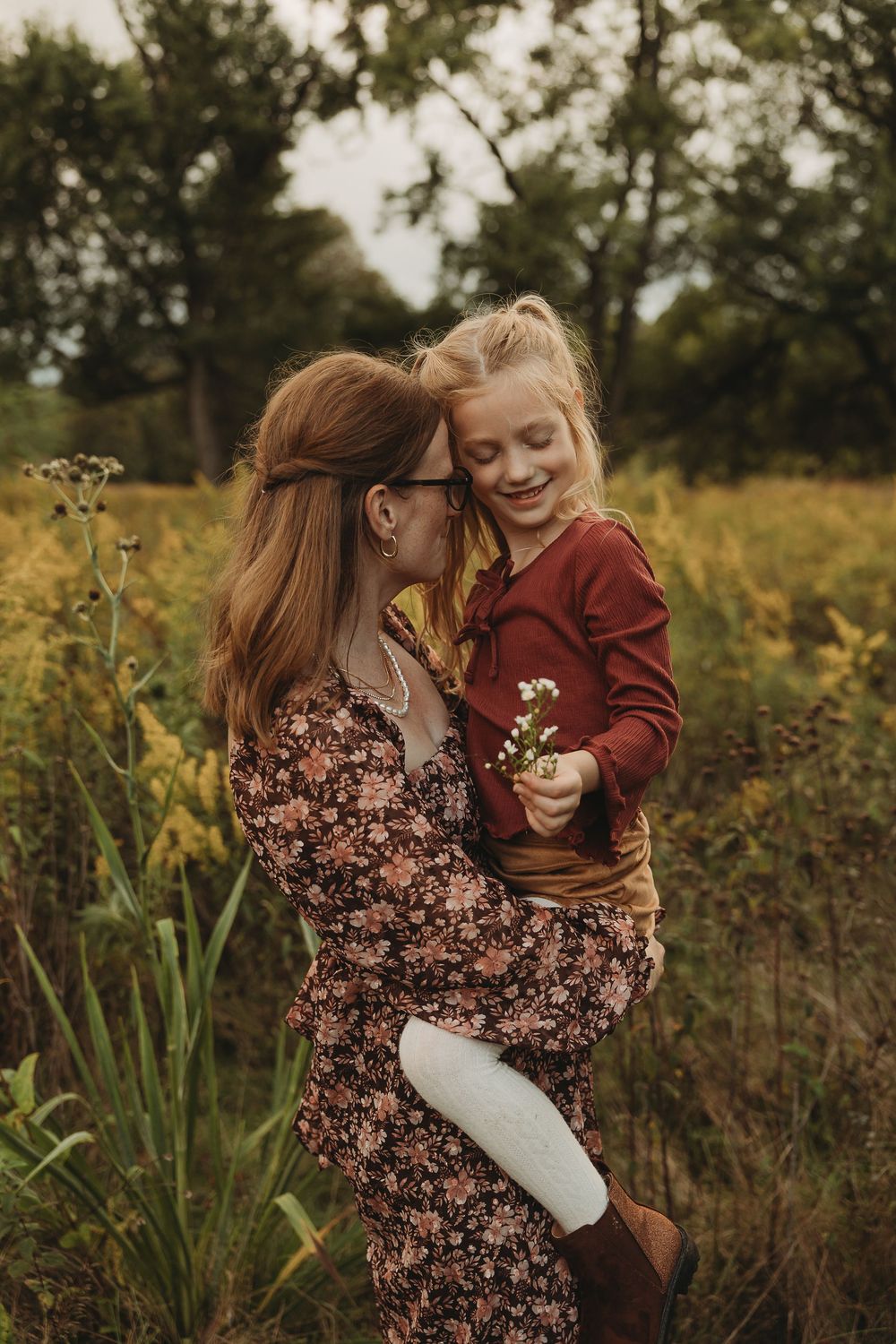 A tender moment captured in a golden autumn field with wildflowers and tall grass at sunset.