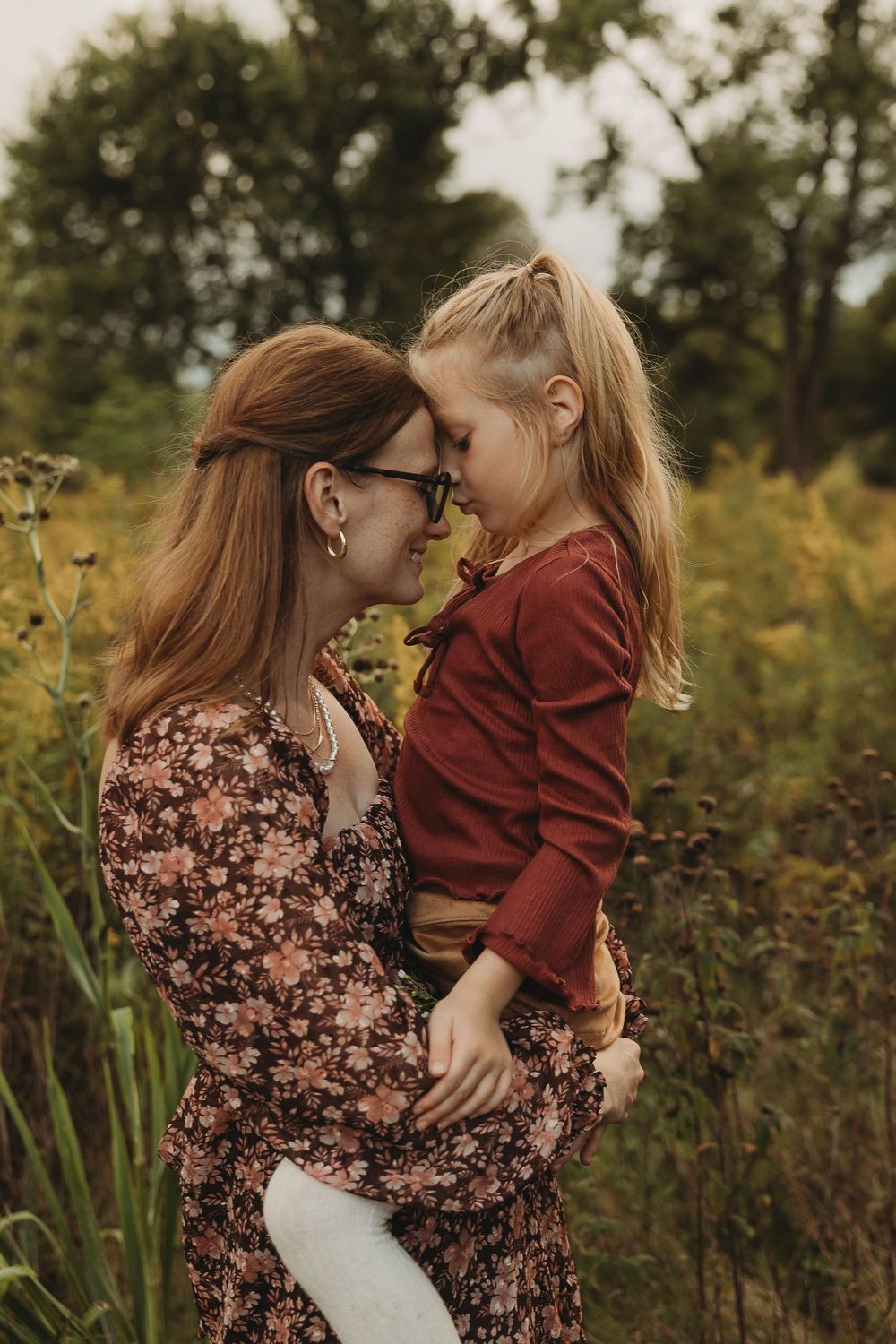 An intimate outdoor portrait showing a tender moment between two people in a natural meadow setting.