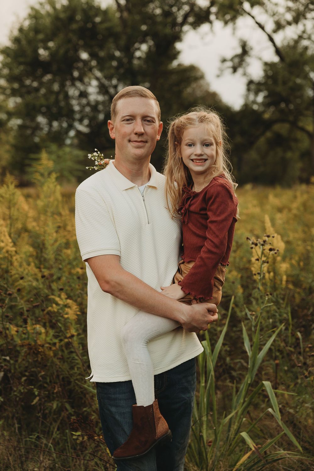 Portrait of two people standing in a golden wildflower field during sunset with natural outdoor lighting.