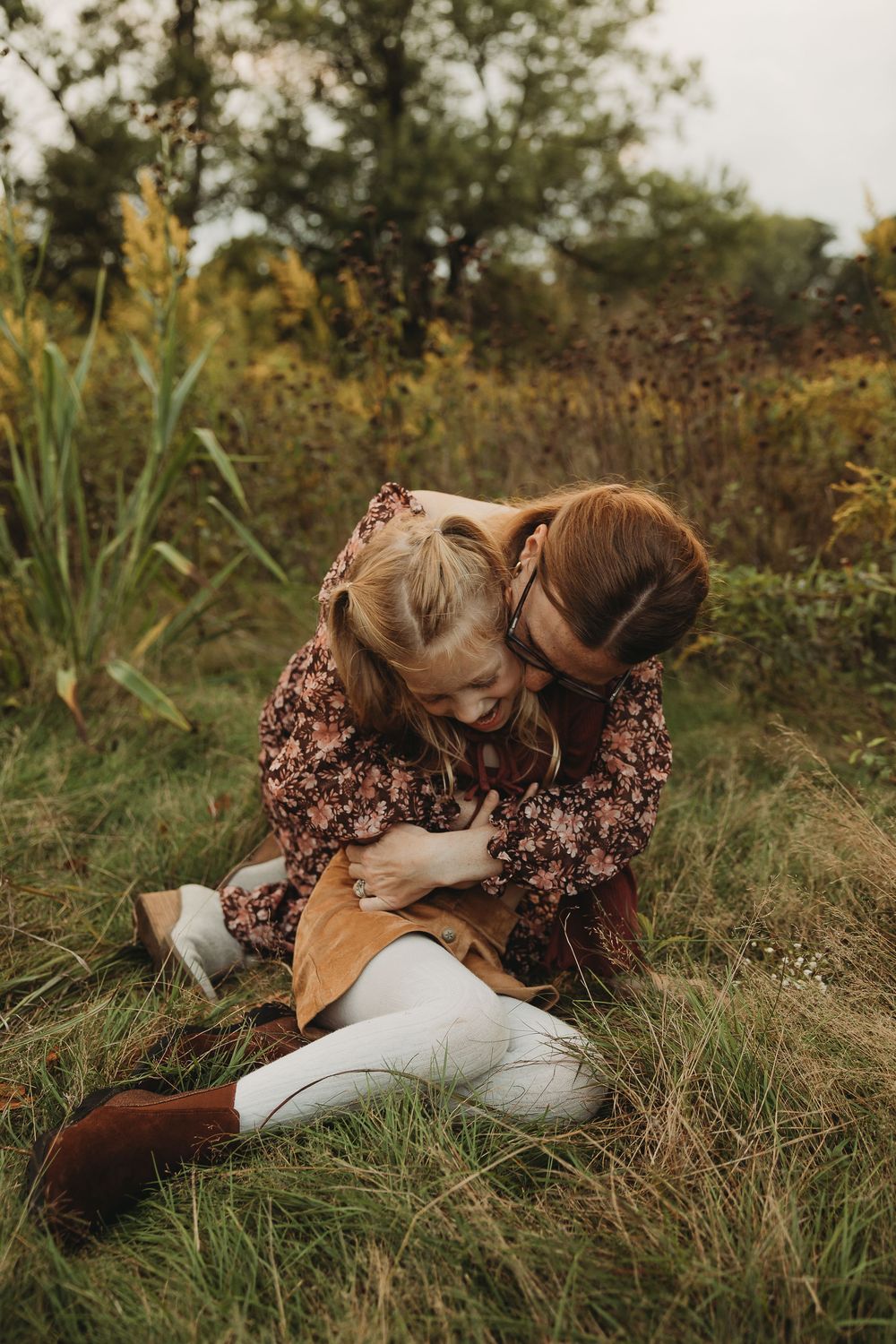 A person wearing a floral dress lies peacefully in tall grass during golden hour.