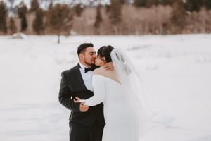 Newlyweds embrace in a snowy winter landscape.