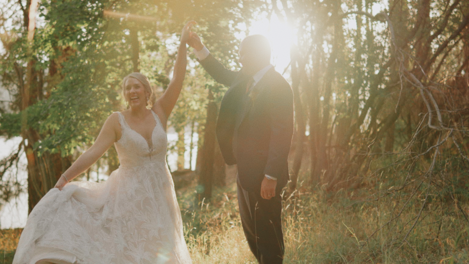 A wedding couple holding hands while walking through a sunlit forest clearing.