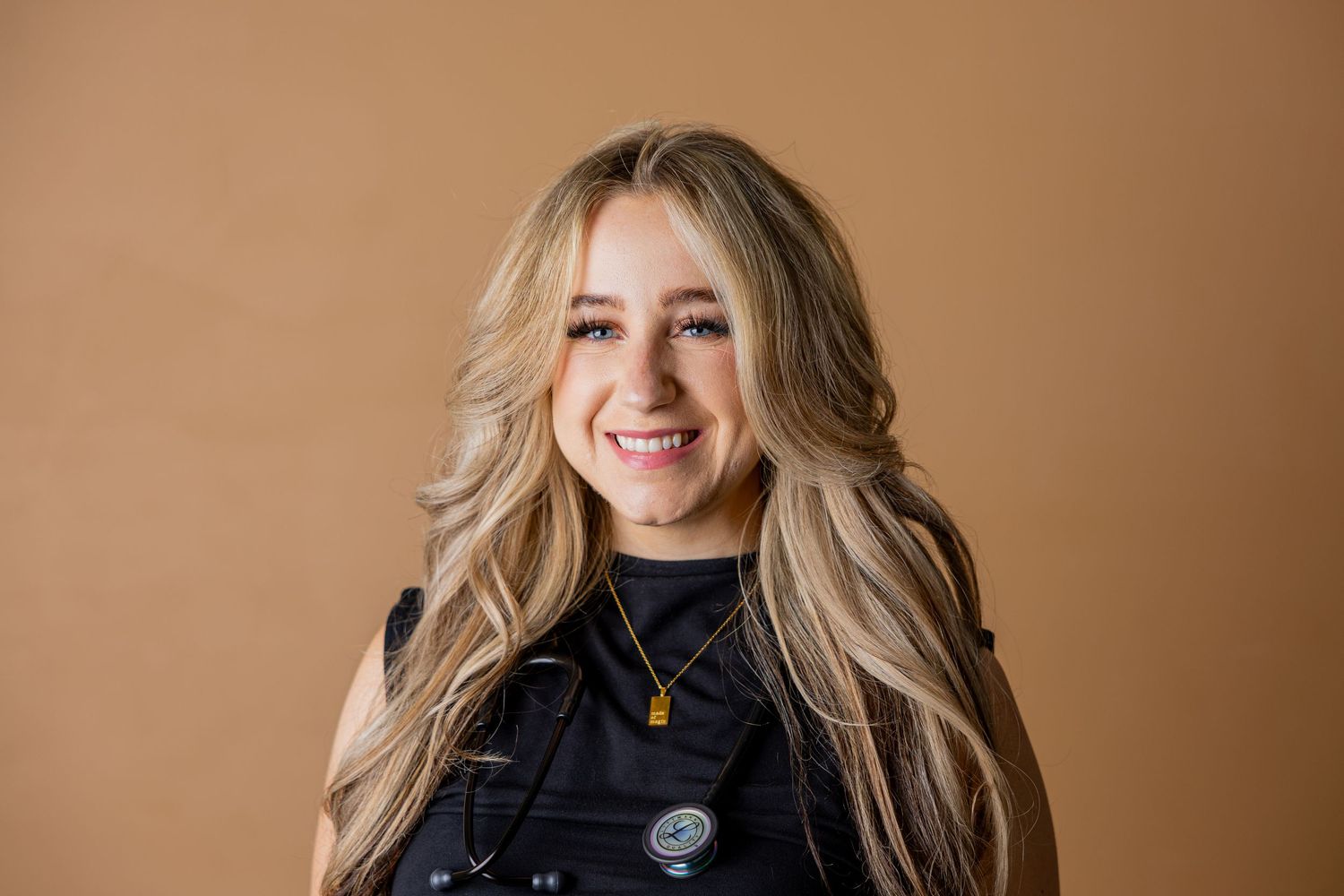 A person wearing a colorful plaid jacket smiles warmly against a white background.