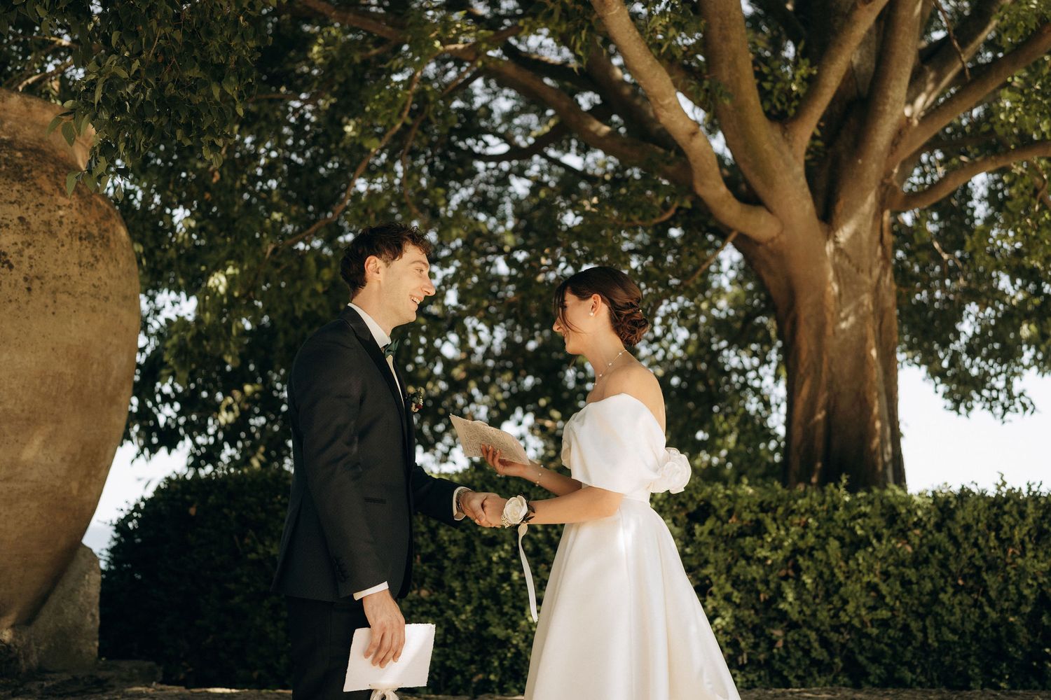 A couple sharing an intimate moment during their wedding ceremony under large trees.