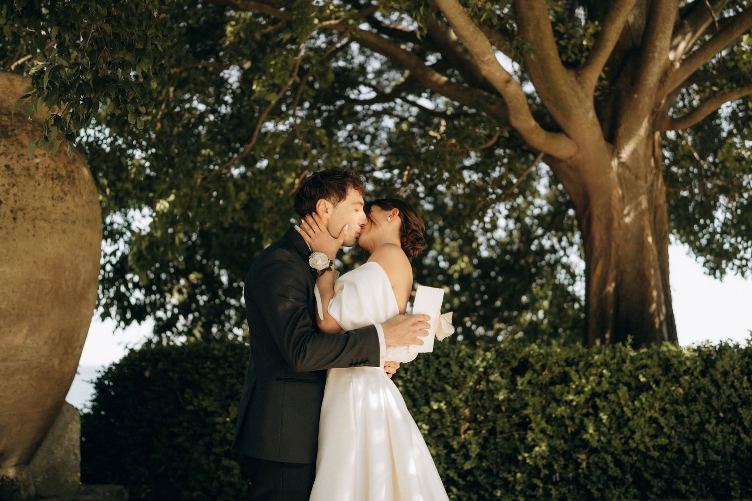Newlyweds embrace and kiss during their outdoor garden wedding ceremony.