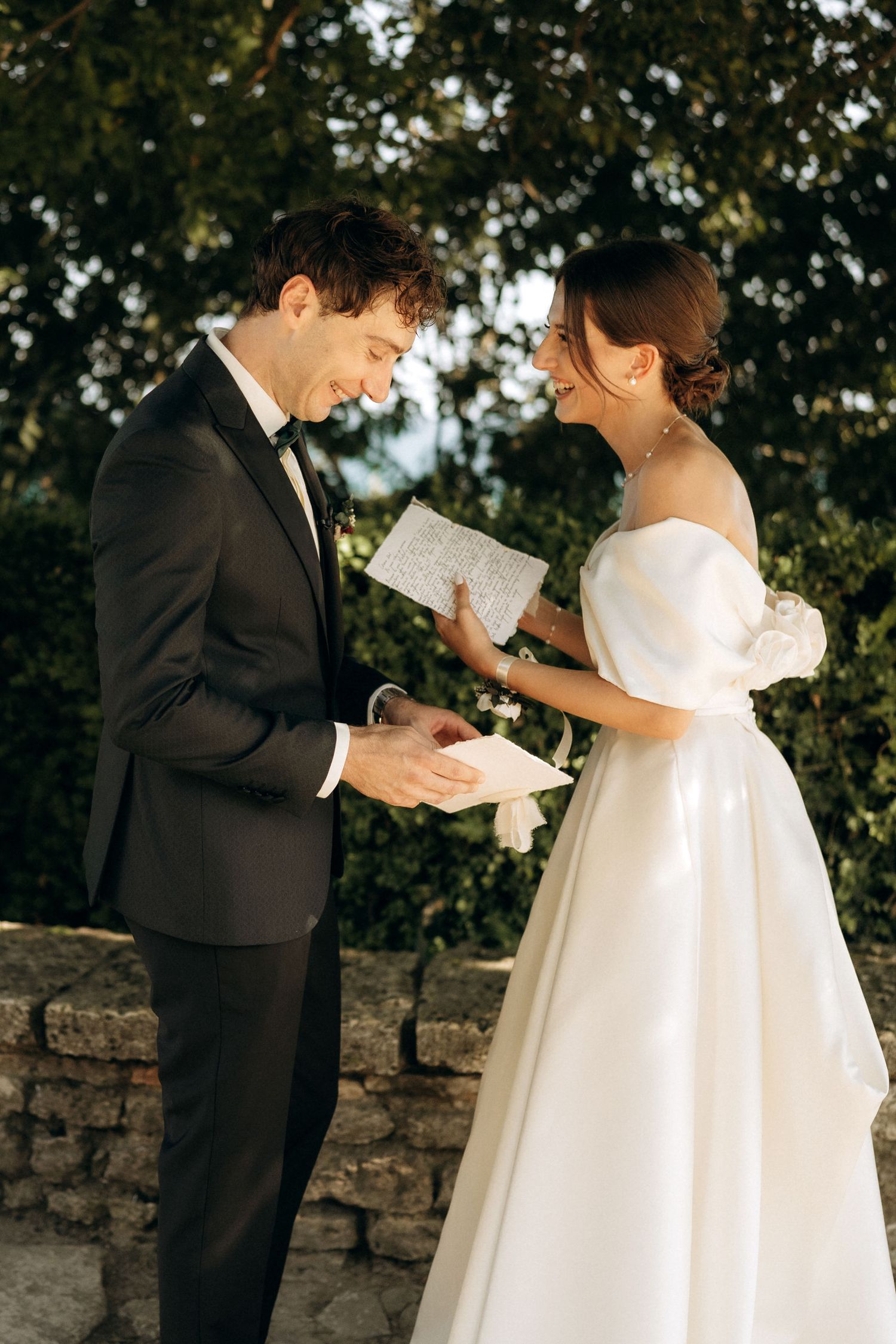 A joyful wedding moment as the couple reads handwritten notes to each other outdoors.