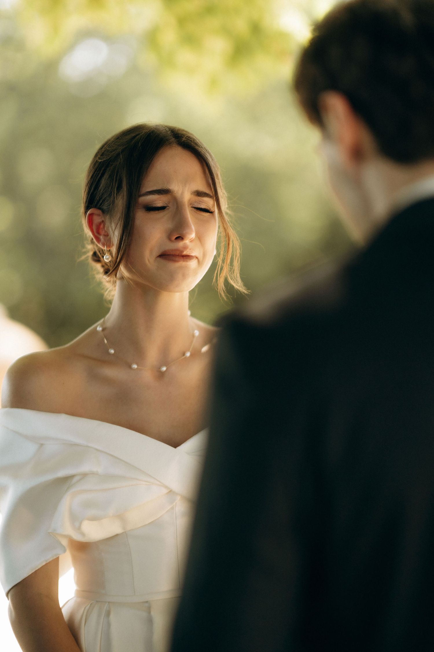 An emotional moment during wedding vows with bride in off-shoulder white dress.