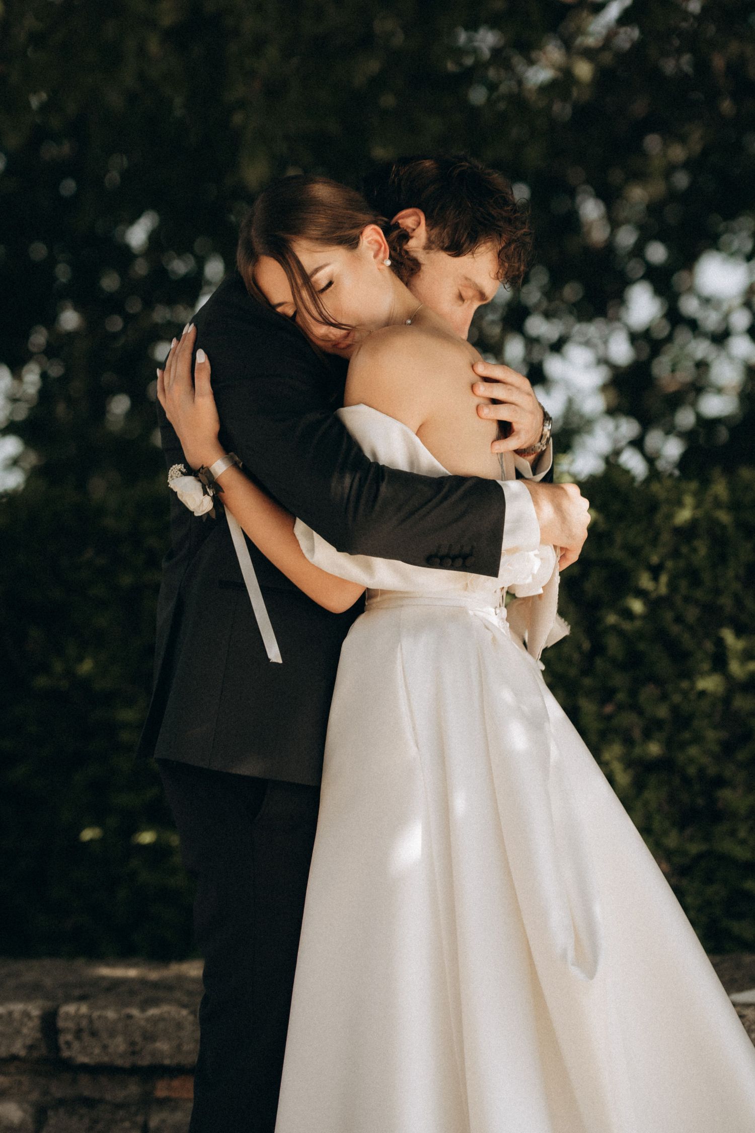 A romantic embrace between a couple in formal wedding attire under natural outdoor lighting.